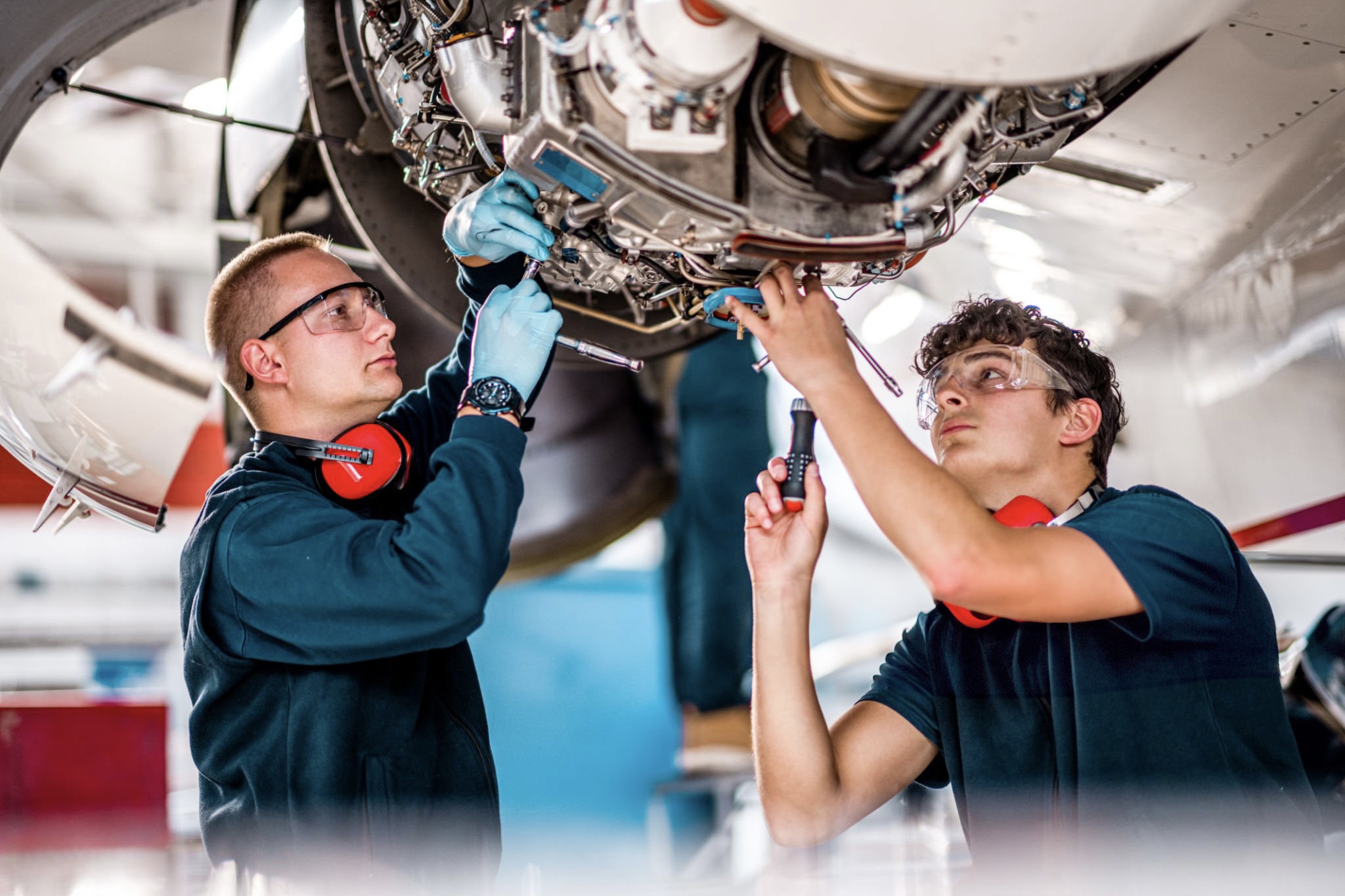 Two young male aircraft maintenance mechanics checking and inspecting an airplane jet engine in the hangar.